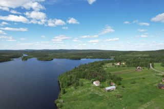 Ylhäältä kuvattu kylämaisema. Edustalla Suinkinkijärvi . Vihreän pellon laidalla pihapiirissä talo ja nevettarakennus. Taustalla kaksi erillistä taloa.